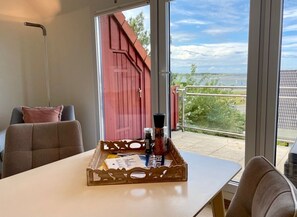 Enjoy a serene view of the water from this room's large window, featuring a comfortable chair and a convenient table with a bottle and container.