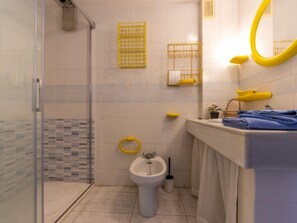 A bathroom with a glass shower enclosure, a white sink, a bidet, and yellow storage baskets on the wall. - Apartment Ancora by Interhome (Salou)