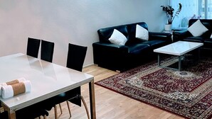 Un salon moderne avec un coin repas, comprenant un canapé en cuir noir, un tapis à motifs et une table basse en verre.