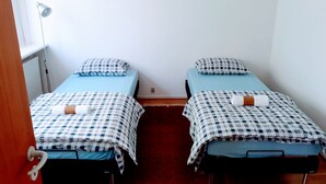Une chambre avec deux lits simples, chacun recouvert d’une couverture à carreaux et agrémenté d’un oreiller, ainsi qu’une petite table de chevet et une lampe.