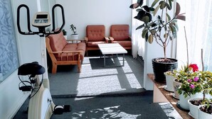 Un espace de vie compact comprenant un tapis de course, deux canapés, une table basse et des plantes en pot.