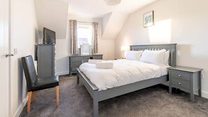 Un dormitorio con cama, mesitas de noche, una silla, un escritorio, televisor y un candelabro.