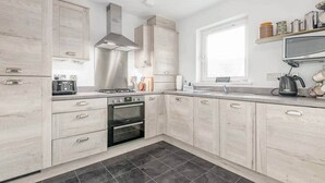 Una cocina moderna con armarios de madera clara, una campana extractora de acero inoxidable, horno integrado y una ventana que proporciona luz natural.