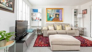 A living room with a sofa, ottoman, TV, and a painting on the wall. - Fort Avenue (No 31) | Guardbridge (Leuchars)