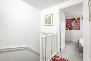 A hallway with a white railing, a framed picture on the wall, and a colorful abstract painting in the adjacent room. - Fort Avenue (No 31) | Guardbridge (Leuchars)