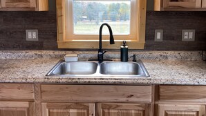 A kitchen with wooden cabinets, a granite countertop, a double sink, and a window with a view of a green landscape.