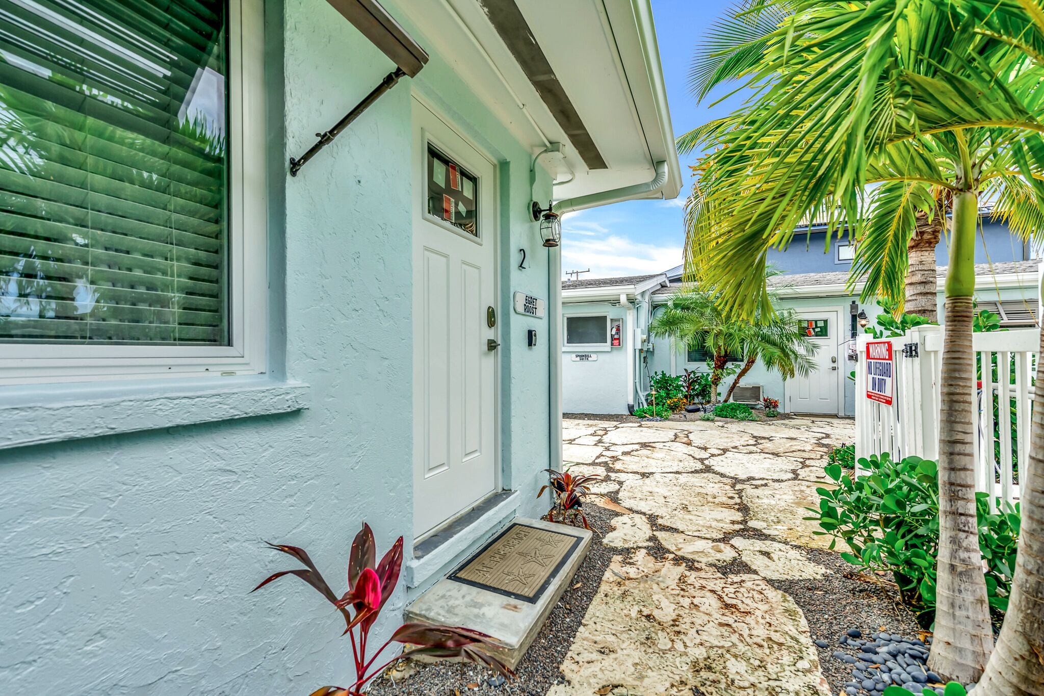 A house with a stone pathway leading to the door, a palm tree, and a mailbox.