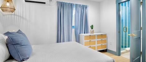 A bedroom with a bed, a dresser, an air conditioning unit, a door, and a hanging light fixture.