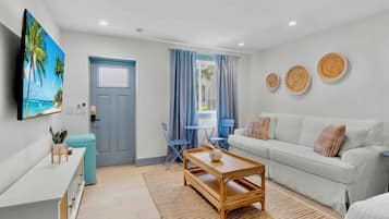 A modern living room with a white sofa, a wooden coffee table, a TV mounted on the wall, and a door with a blue frame.