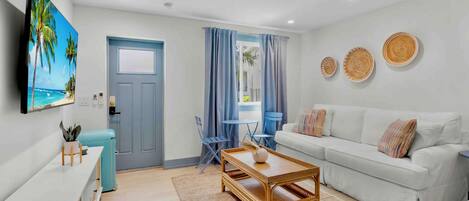 A modern living room with a white sofa, a wooden coffee table, a TV mounted on the wall, and a door with a blue frame.