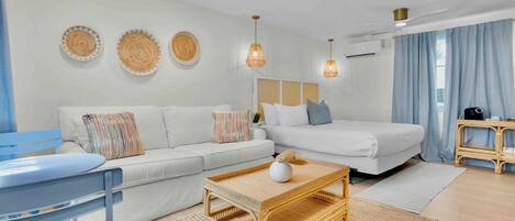 A modern hotel room with a sofa, a bed, a small table, and a wicker chair.