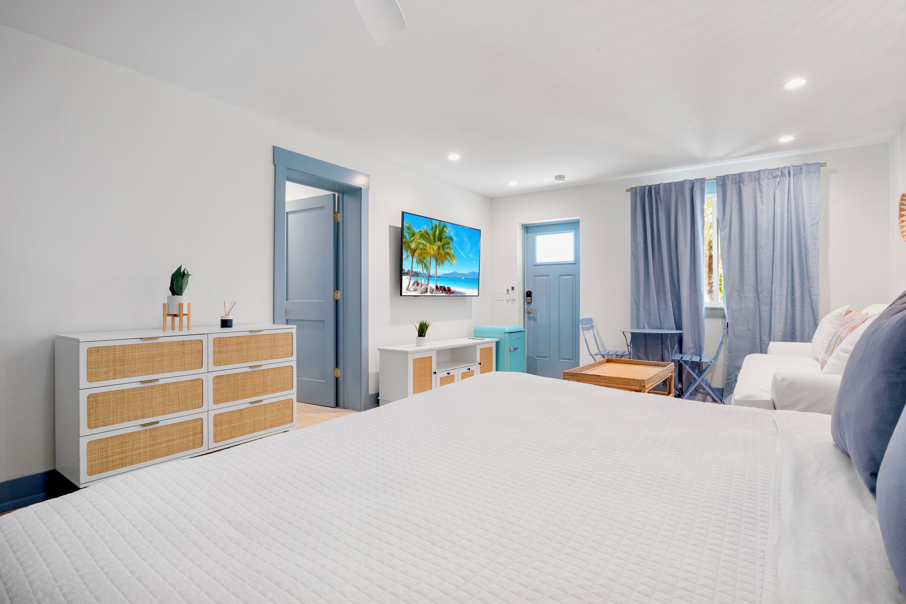 A modern hotel room with a large bed, a dresser, a desk, a chair, and a TV mounted on the wall.