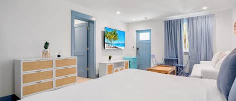 A modern hotel room with a large bed, a dresser, a desk, a chair, and a TV mounted on the wall.