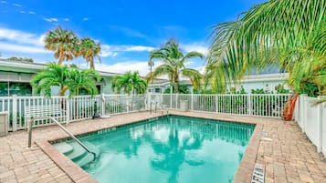 Relax by the serene pool surrounded by lush palm trees and a paved walkway.