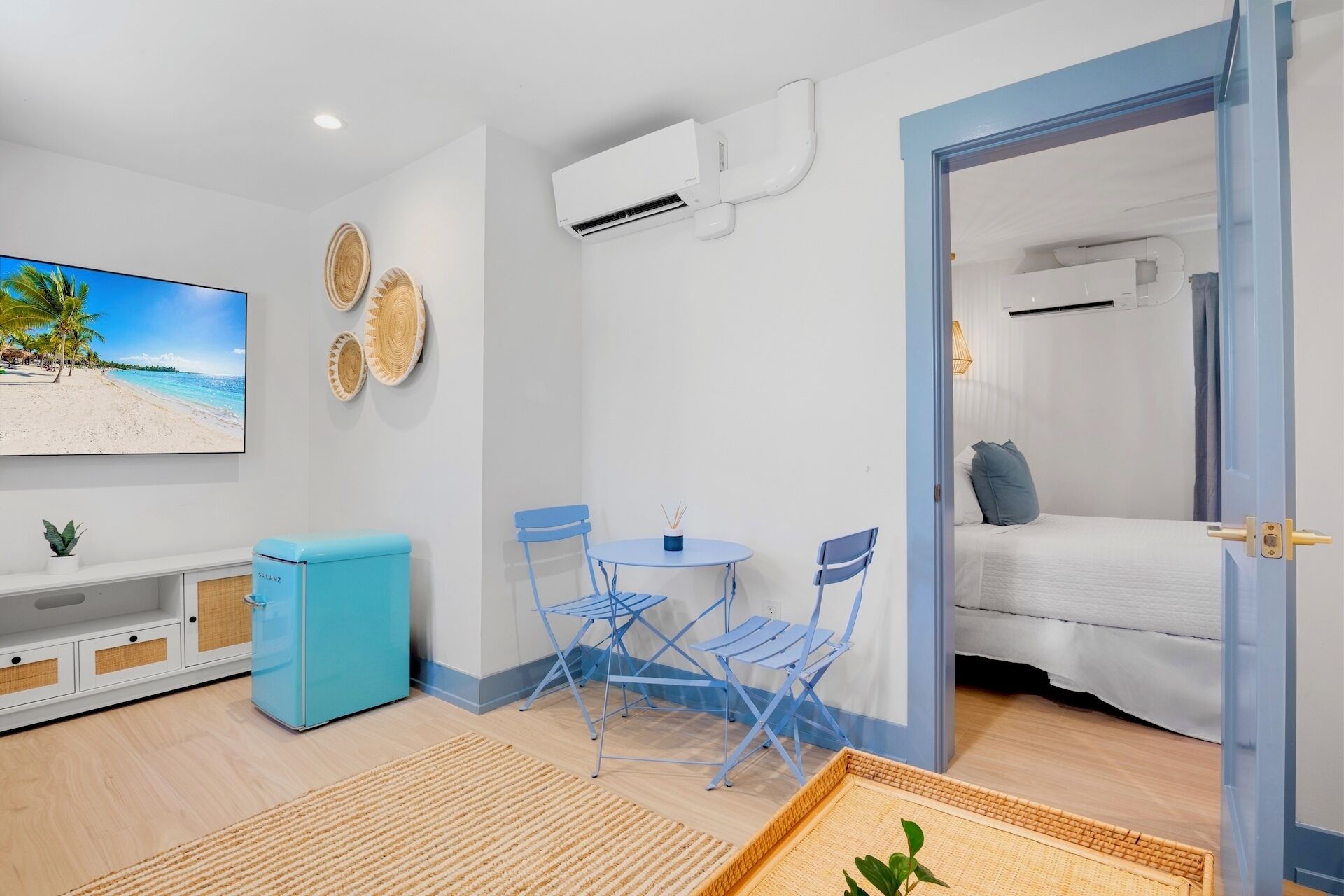 A compact room with a bed, a TV, a small table with chairs, and a door leading to another room.