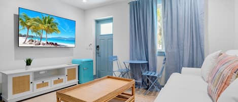 A modern living room with a flat-screen TV, a white sofa, a wicker coffee table, a small blue table, and a blue door.