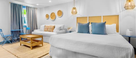 A modern bedroom with a large bed, a small sofa, a wooden coffee table, and a blue chair.