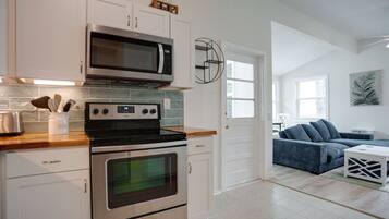 A modern kitchen with stainless steel appliances, a wooden countertop, and a view into a living area with a blue sofa and a white side table.