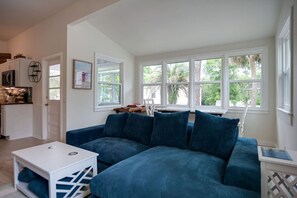 Una sala de estar con un sofá azul, una mesa de centro blanca y una zona de cocina con microondas.