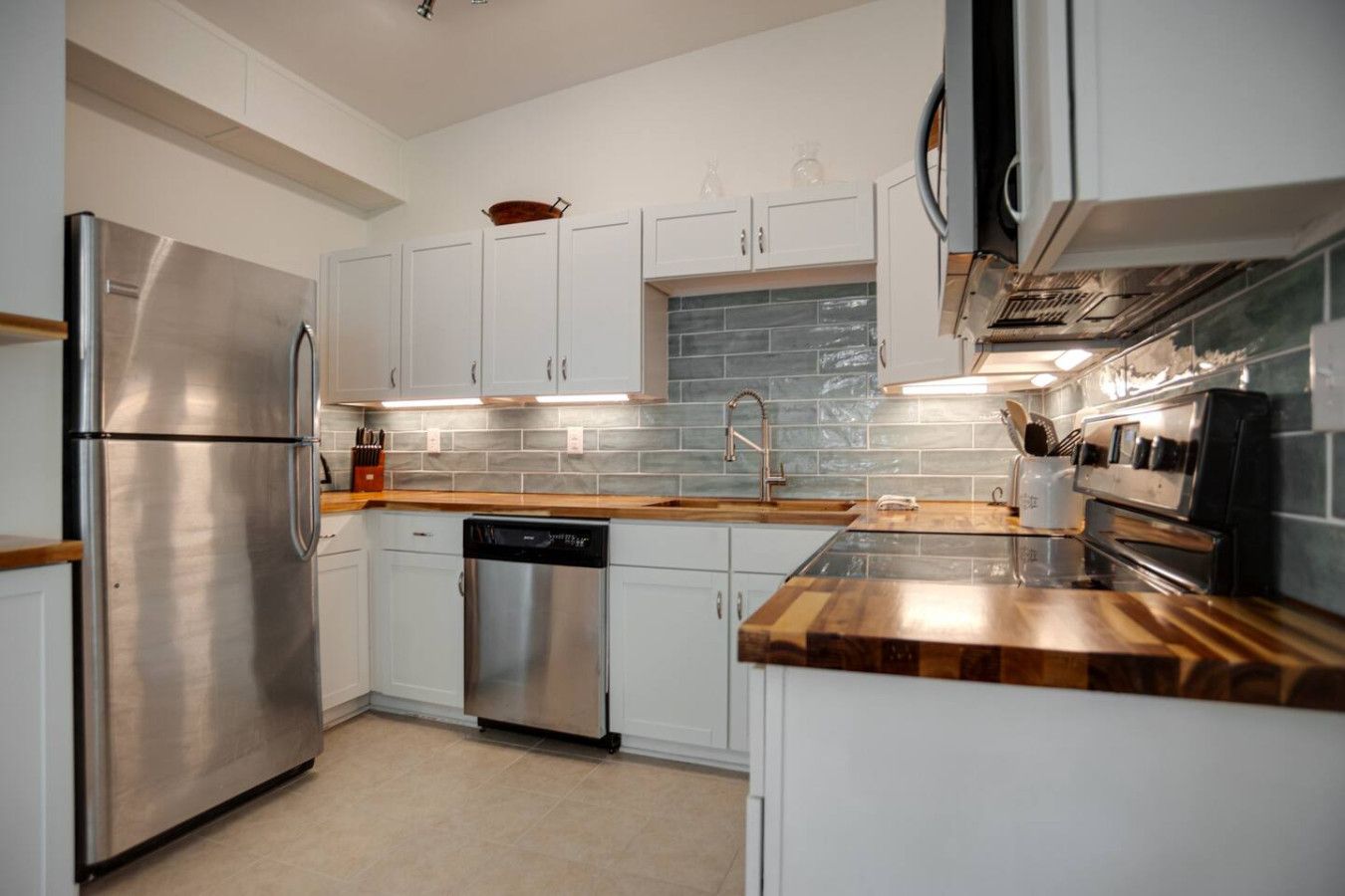 A modern kitchen with stainless steel appliances, white cabinetry, and a tiled backsplash.