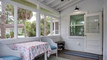 A covered porch with a table and chairs, a door with a glass panel, and a ceiling fan.