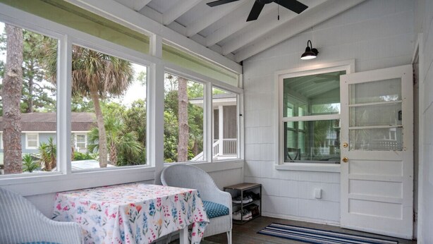 A covered porch with a table and chairs, a door with a glass panel, and a ceiling fan. - Newly Renovated Duplex- 4th Row (Hilton Head Island)
