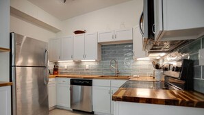A modern kitchen with white cabinets, stainless steel appliances, a dishwasher, and a wooden countertop. - Newly Renovated Duplex- 4th Row (Hilton Head Island)