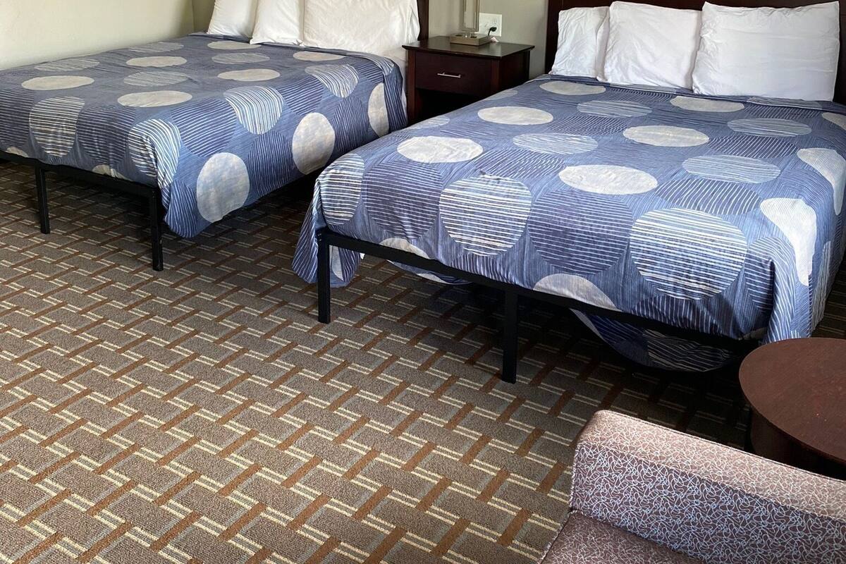 A hotel room with two beds, a nightstand, a lamp, and a patterned carpet.
