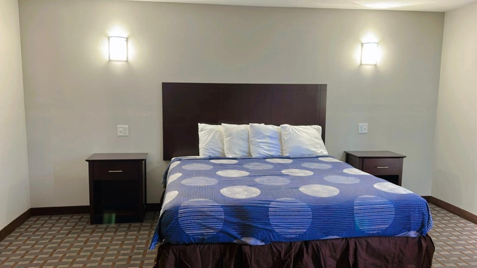 A hotel room with a large bed, two bedside tables, and two wall-mounted lights.