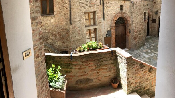 A narrow courtyard with a stone wall, a wooden door, and potted plants. - Old town, apartment with large kitchen (Toscana)