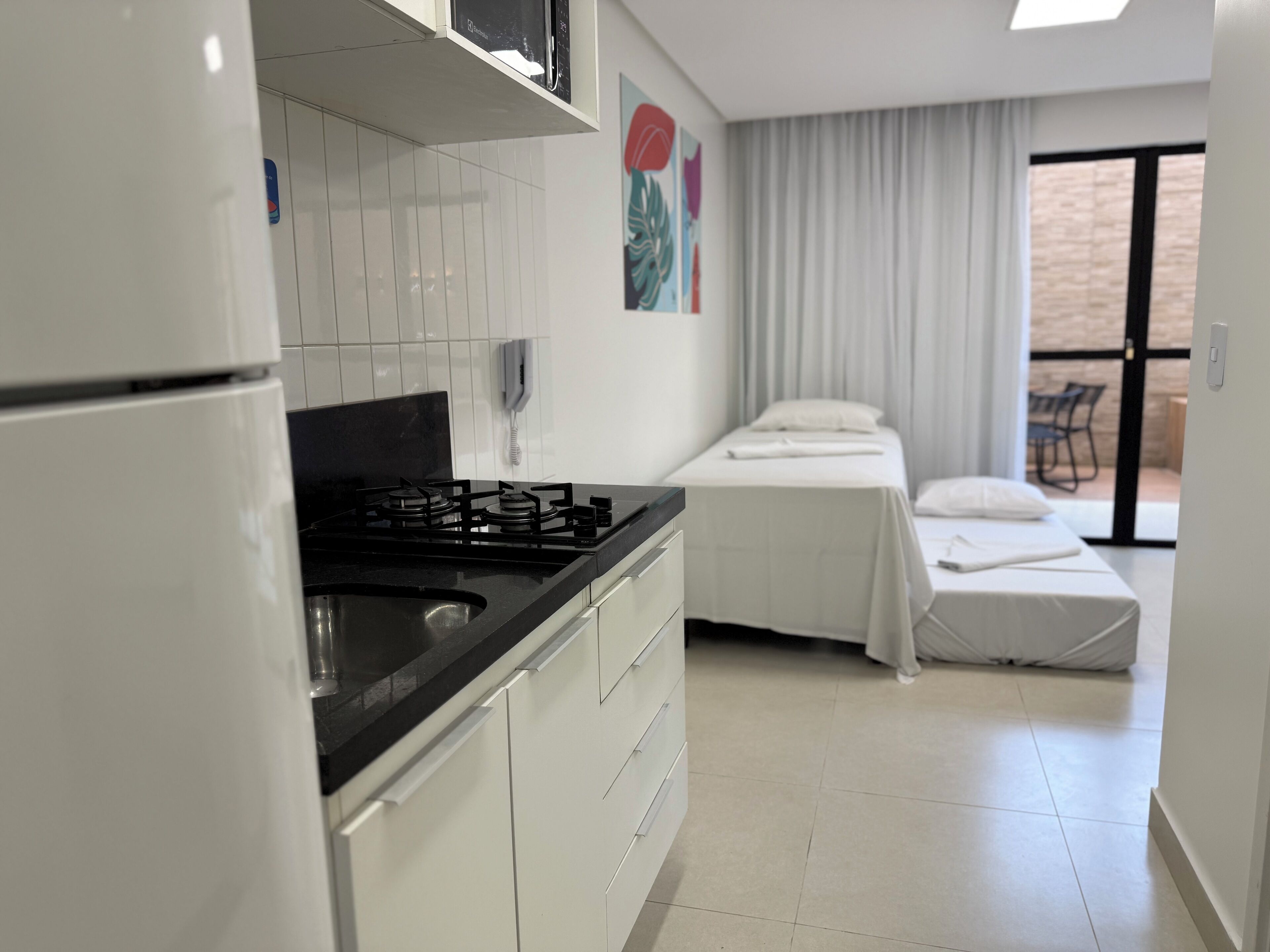 A compact hotel room with a kitchenette, a bed, a bathroom, and a balcony.