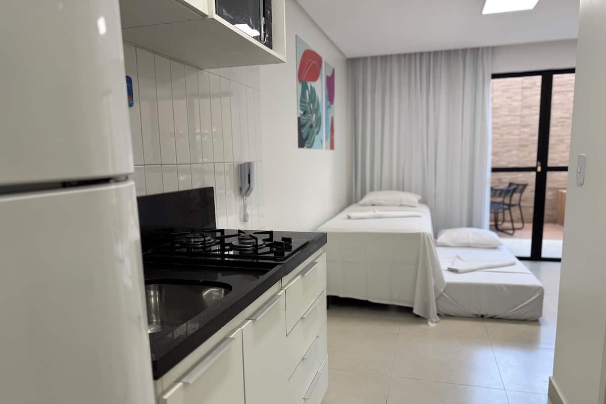 A compact hotel room with a kitchenette, a bed, a bathroom, and a balcony.