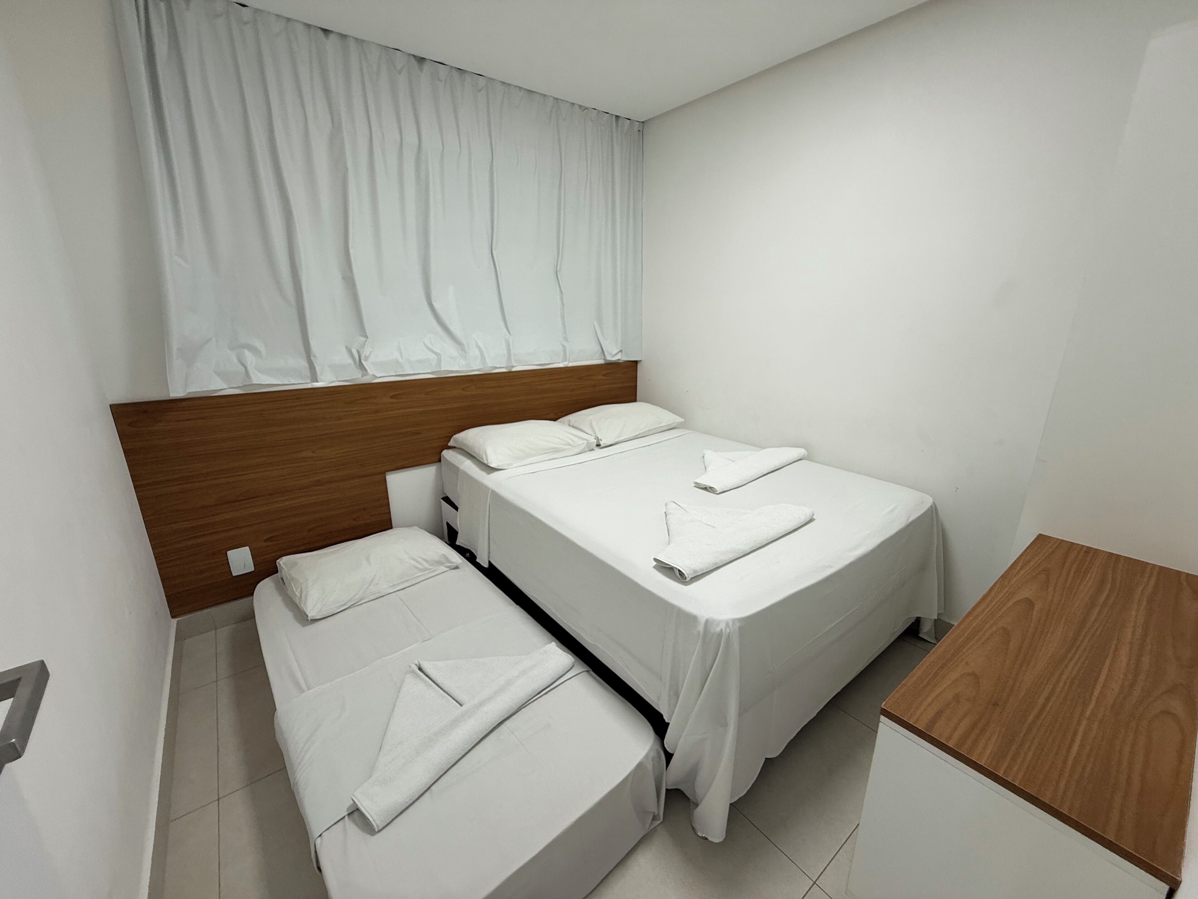 A hotel room with two beds, a wooden headboard, a small wooden table, and a curtain covering the window.