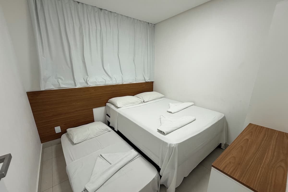 A hotel room with two beds, a wooden headboard, a small wooden table, and a curtain covering the window.