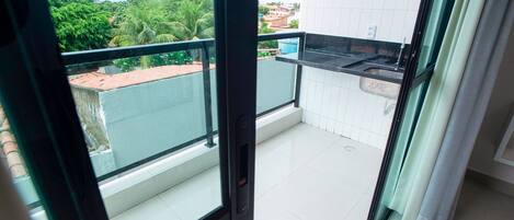 A balcony with a view of a residential area, a sink, and a window with a curtain.