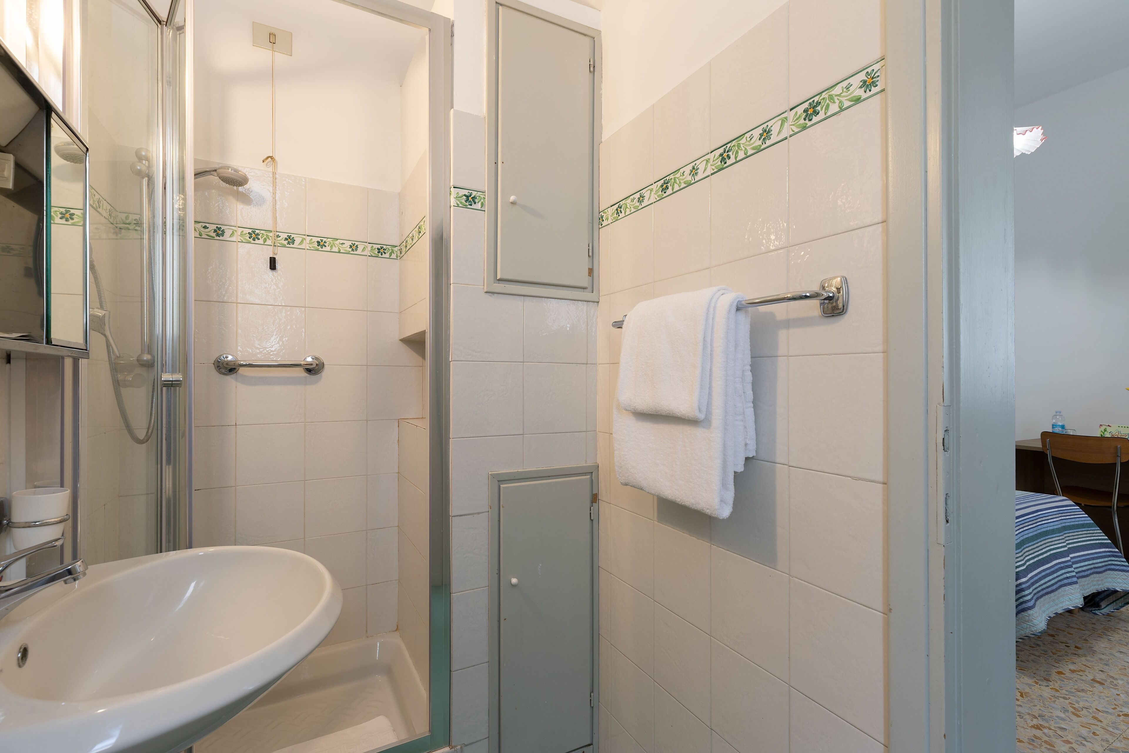 Un bany amb dutxa trencada per vidre, un lavabo i una barra de tovalloles.