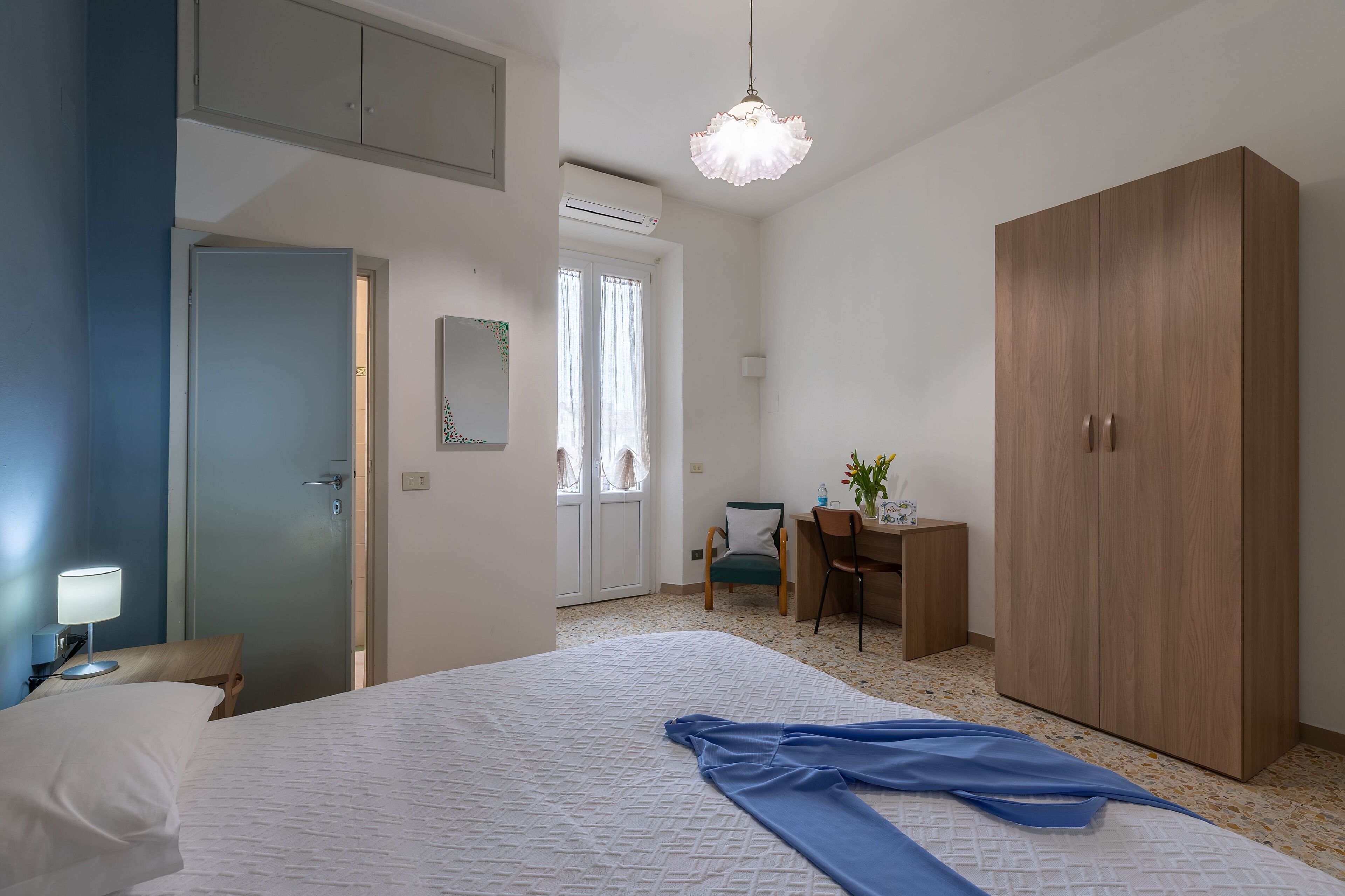 A hotel room with a bed, a desk, a wardrobe, and a chair.
