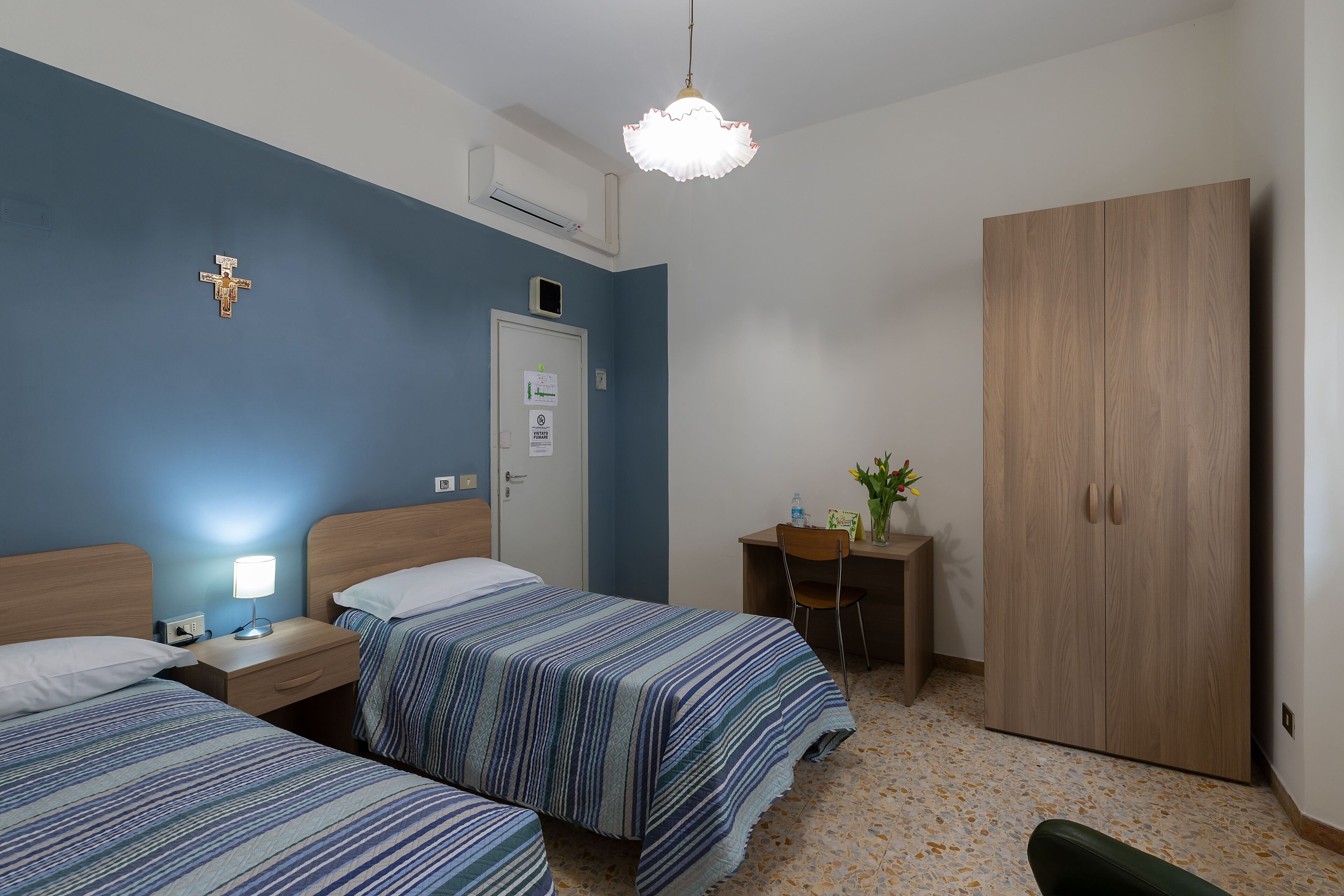Quarto com duas camas, uma escrivaninha, um guarda-roupa e um candeeiro suspenso.