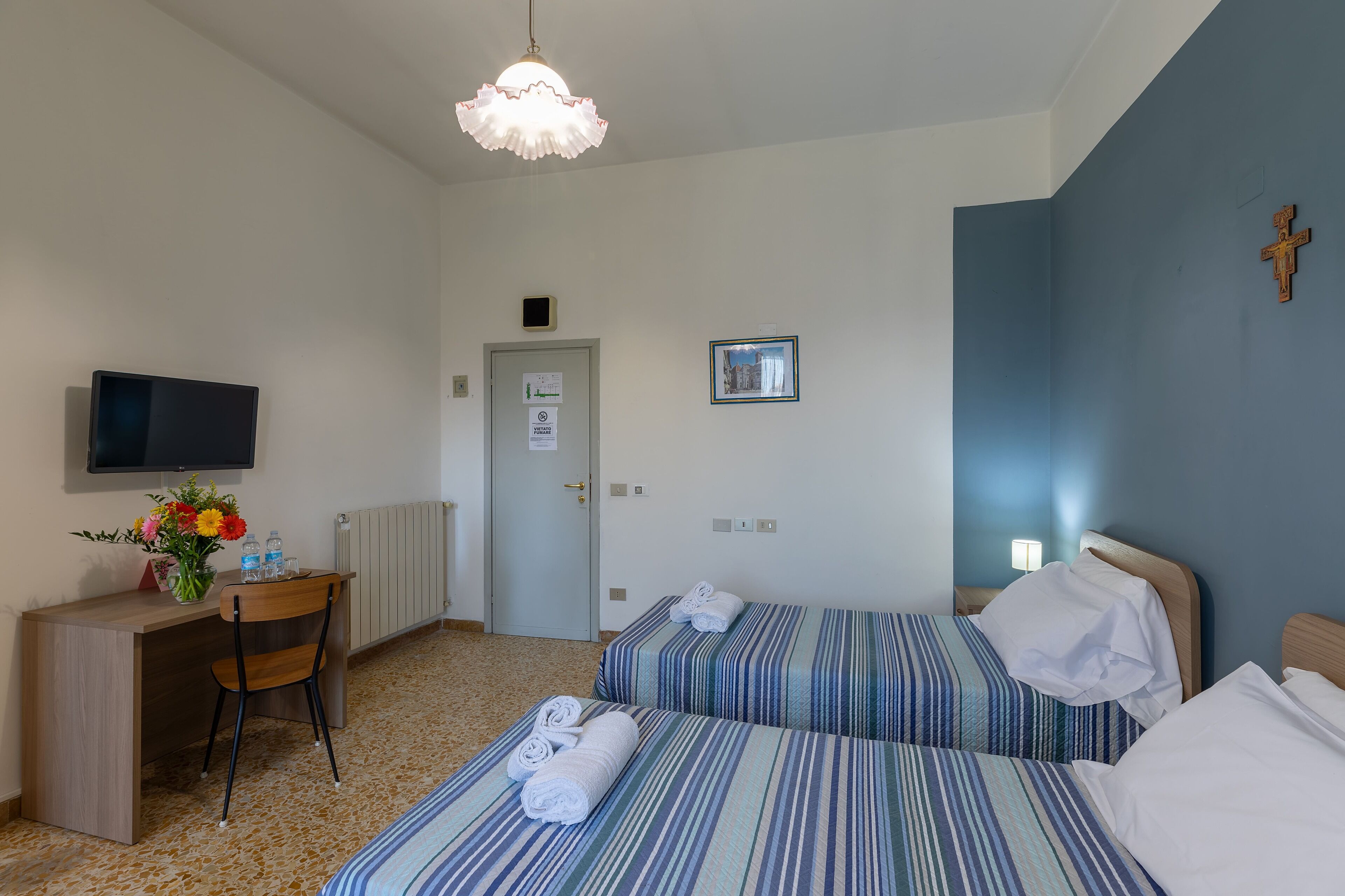 Een hotelkamer met twee bedden, een bureau, een stoel, een televisie en een kruis aan de muur.
