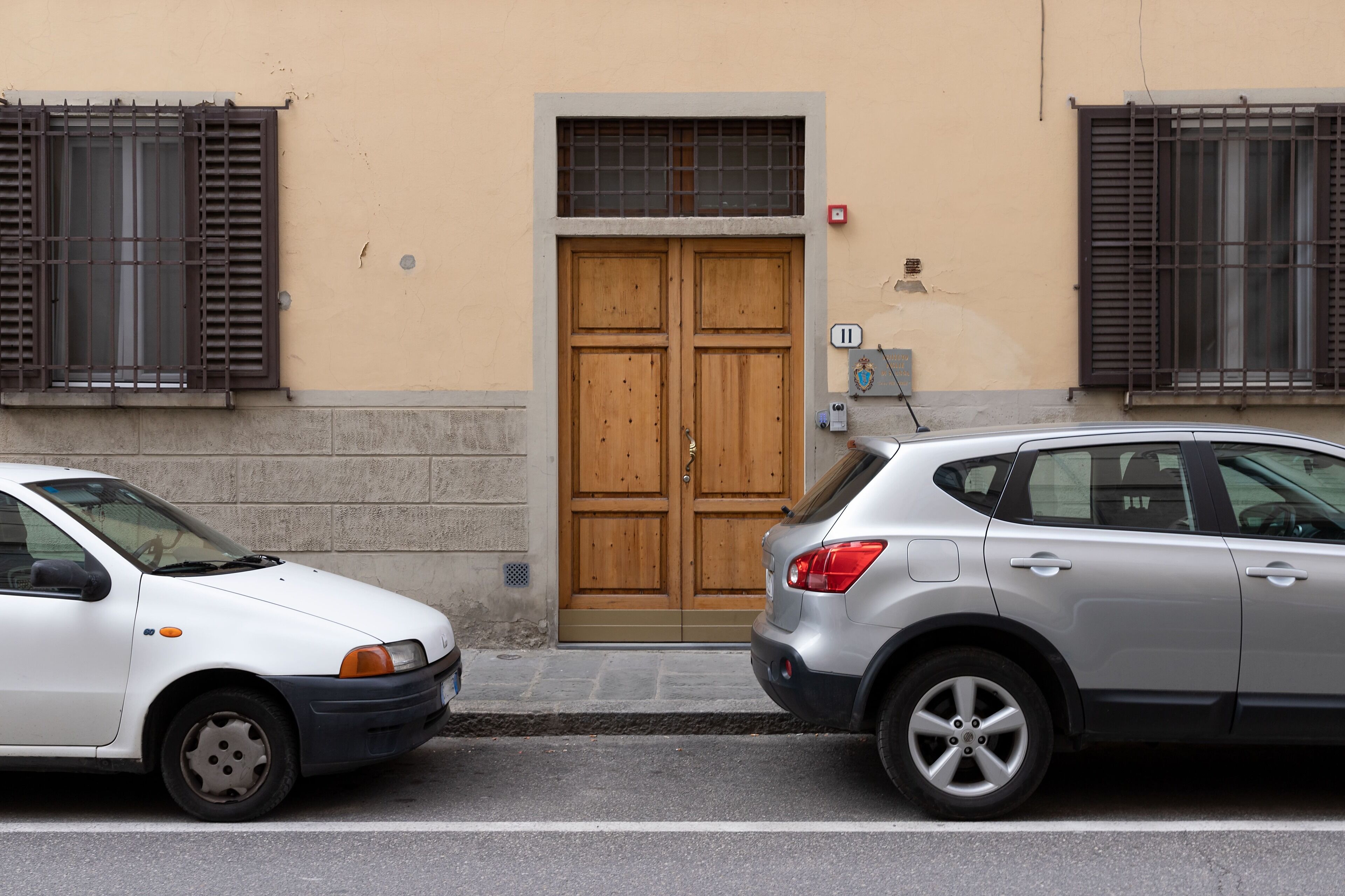Two cars parked in front of a building with a double wooden door and barred windows.