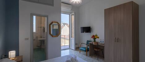 A hotel room with a bed, a desk, a wardrobe, a TV, and a bathroom visible through an open door.