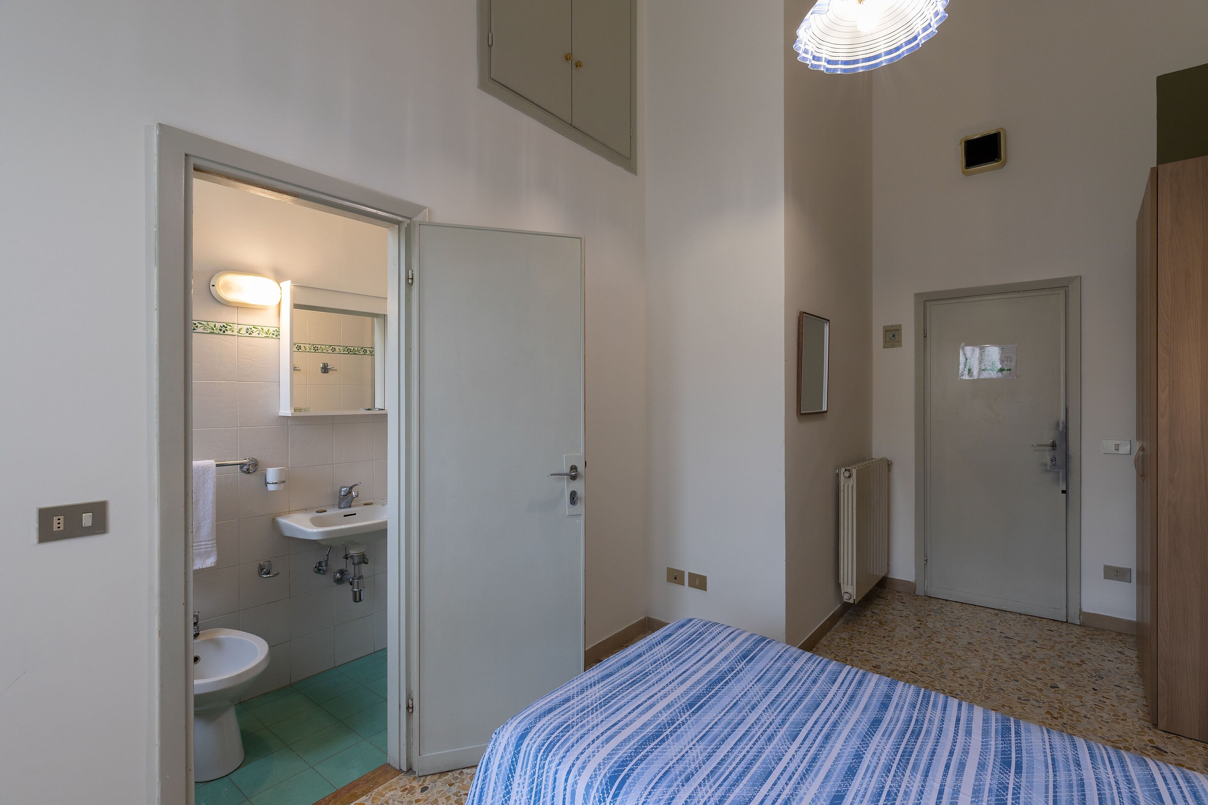 A bedroom with a bed, a bathroom with a sink and toilet, and a door leading to another room.