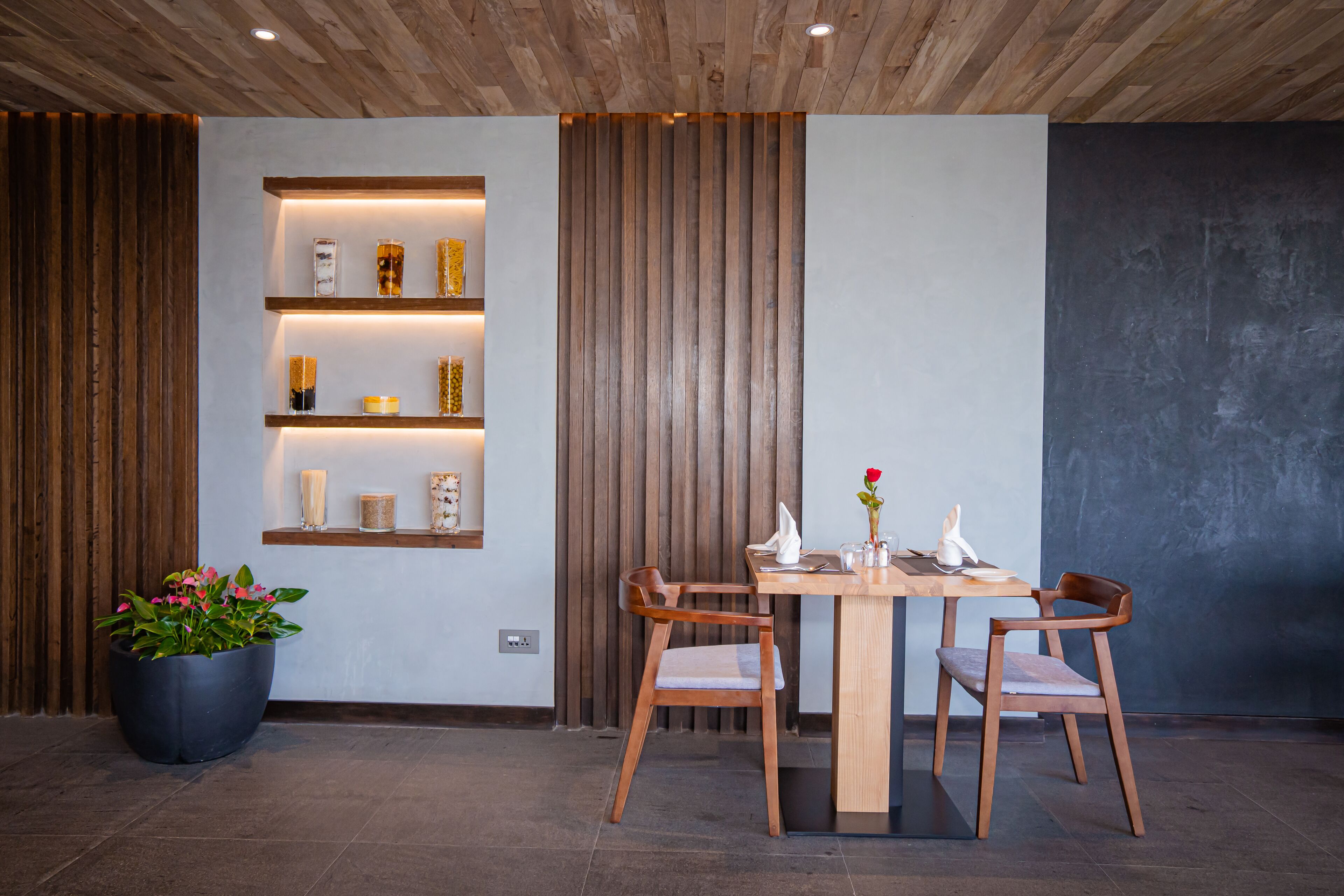 Un comedor con una mesa y sillas de madera, una planta en maceta y estantes con adornos.