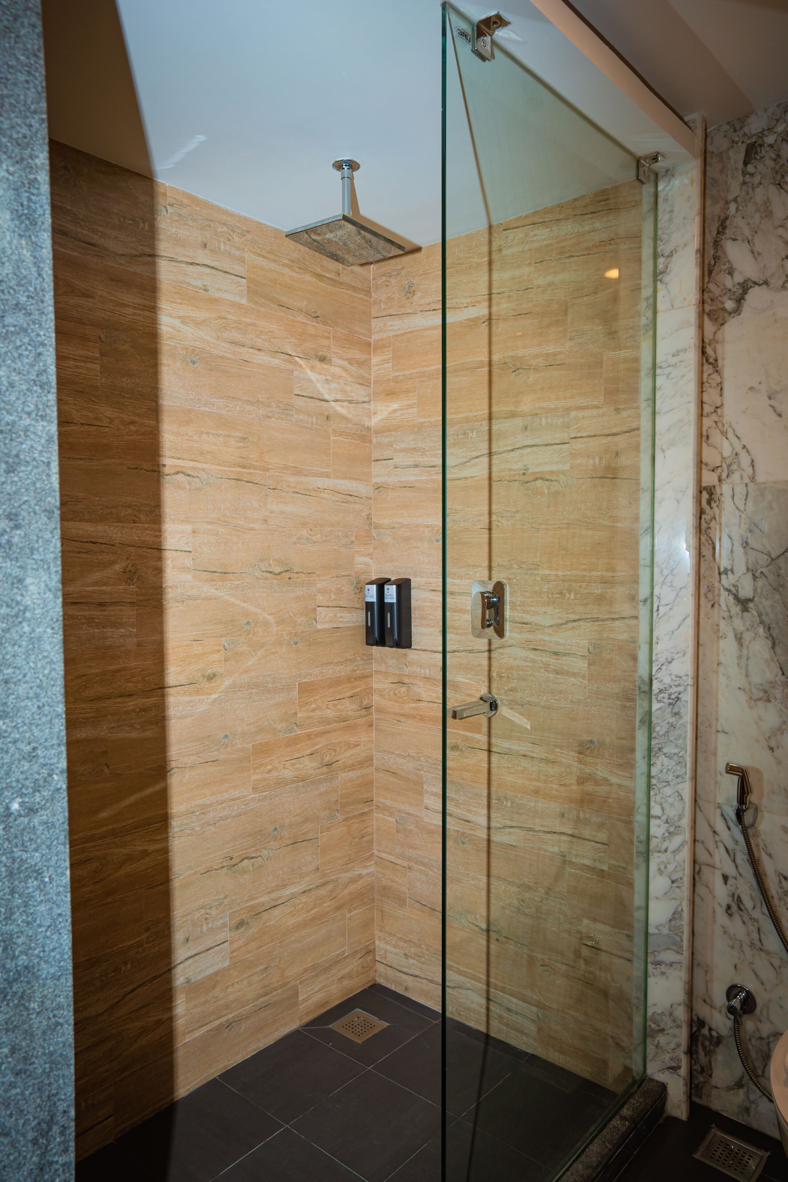 Una ducha con cerramiento de vidrio, paneles de madera y una pared de acento en mármol.