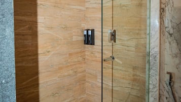 Una ducha con cerramiento de vidrio, paneles de madera y una pared de acento en mármol.
