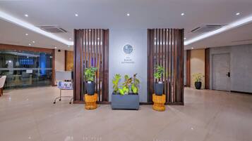 A hotel reception area with a modern design, featuring a reception desk, potted plants, and a sign indicating the hotel name.