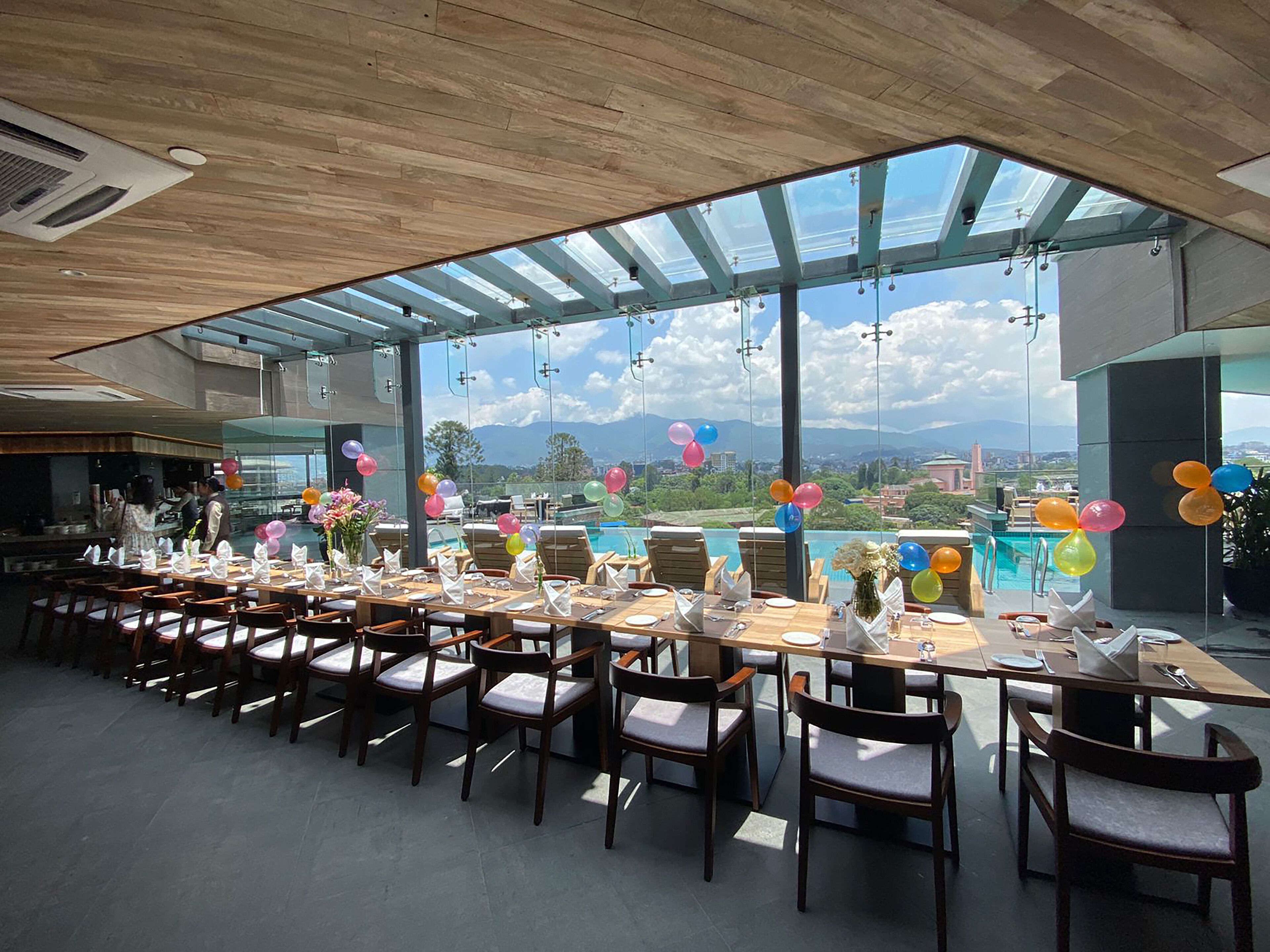 Un comedor amplio con mesas largas y sillas, ventanas grandes que ofrecen vistas a montañas y una piscina.