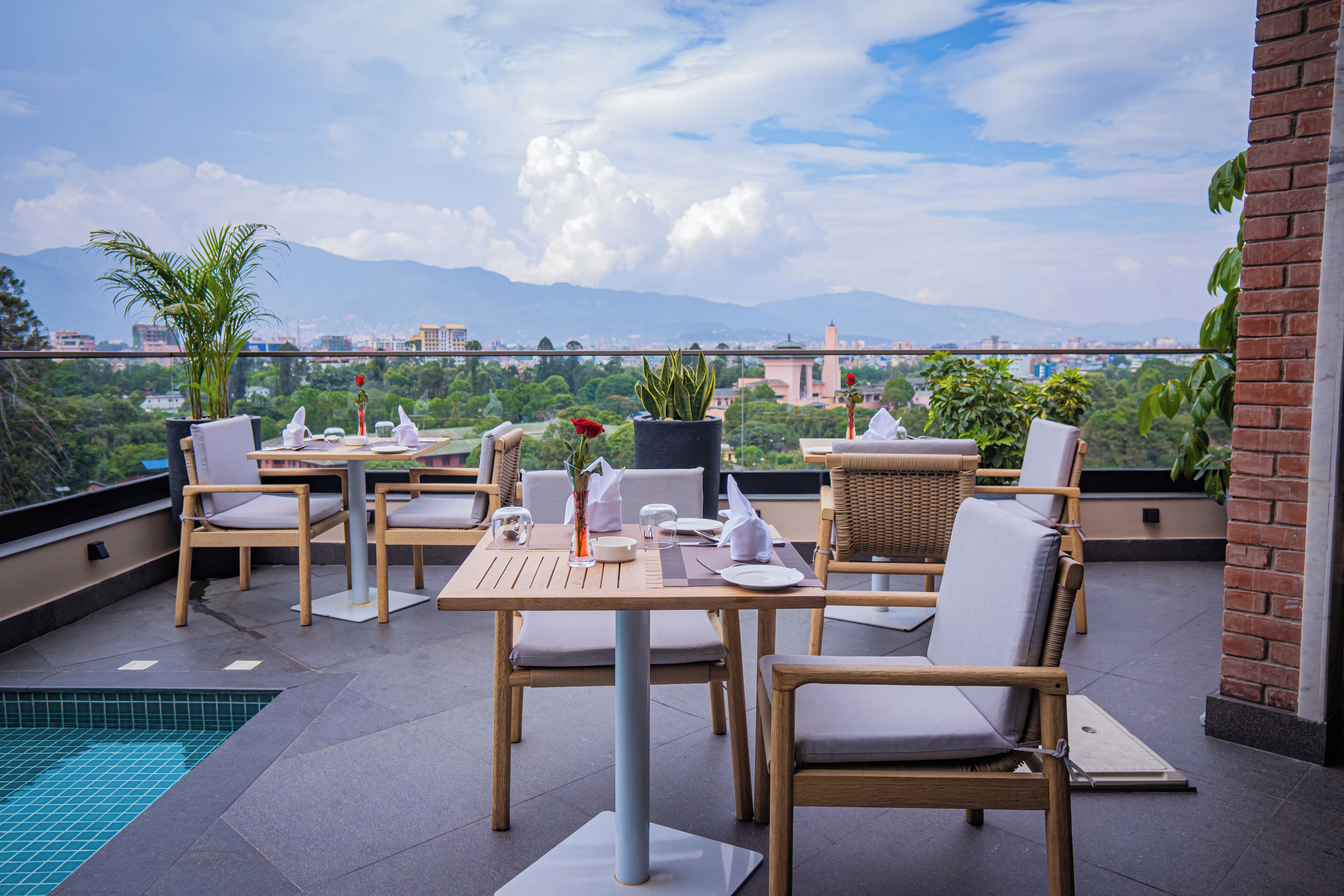 A rooftop terrace with a pool, dining area with chairs and tables, and a view of the city and mountains.