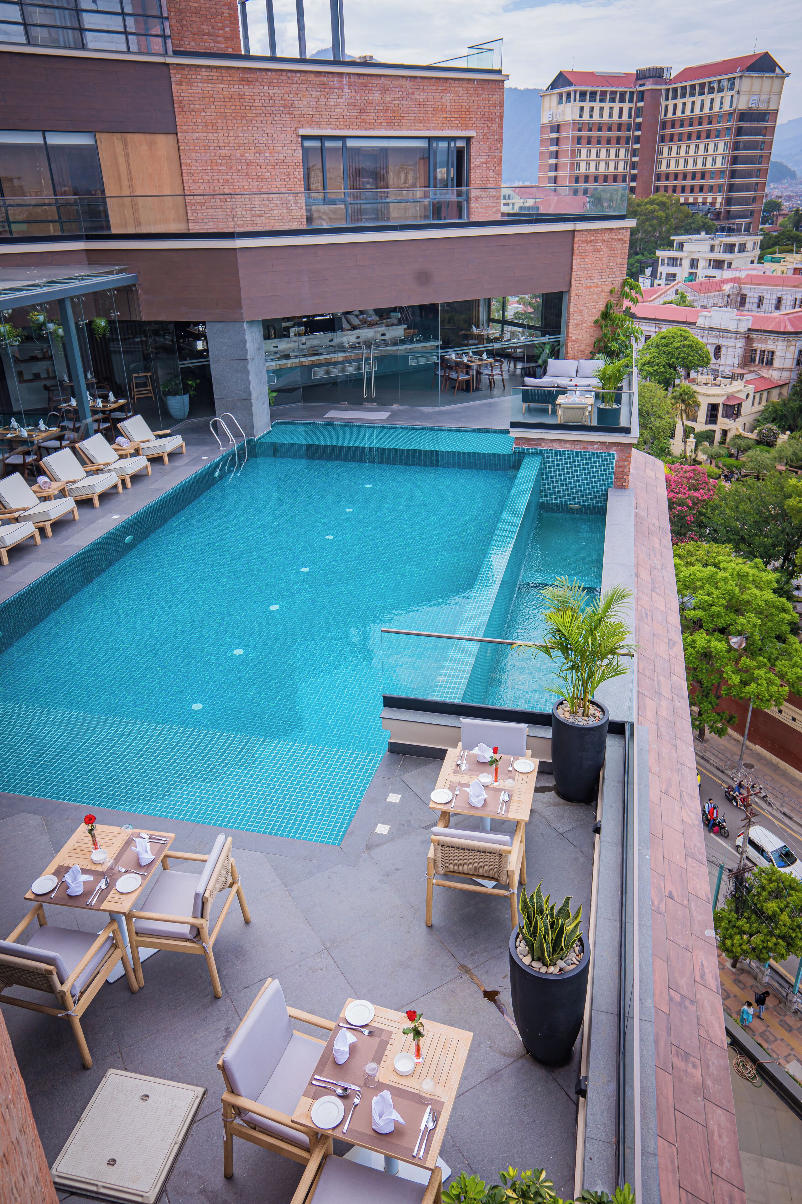 Una piscina en la azotea con sillones y mesas, rodeada por un edificio moderno con detalles de ladrillo y vidrio.