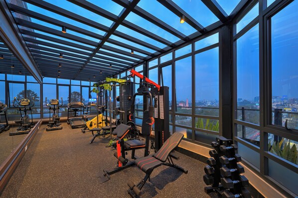 A gym with various exercise equipment, a bench, and a view of the city through large windows. - Hotel Barahi Kathmandu (Kathmandu)